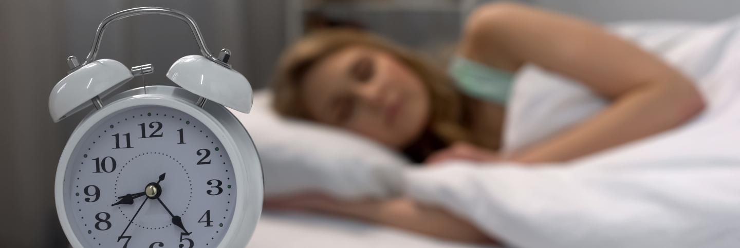 Woman sleeping with alarm clock in foreground